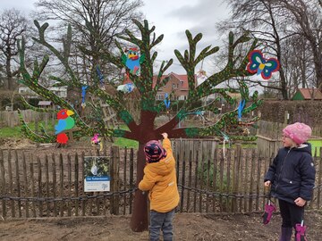 Een kind hangt zijn tutje op aan de tuttenboom in de kinderboerderij.