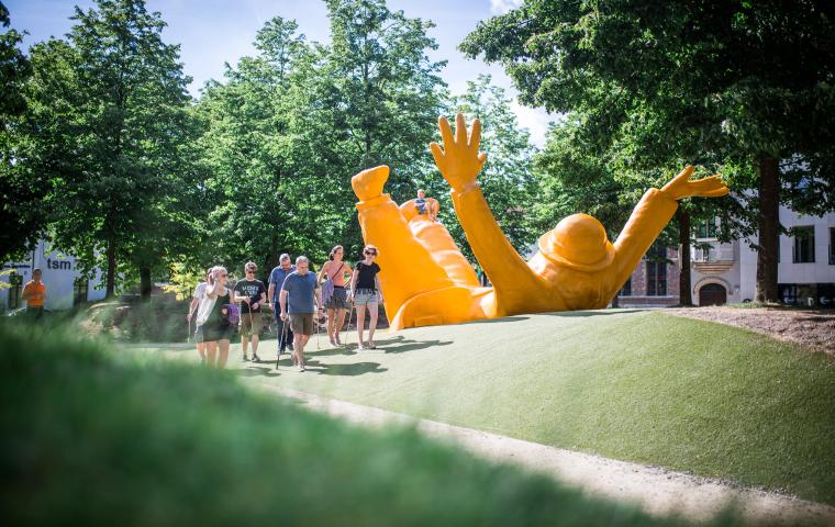 Mensen wandelen voorbij een grote gele Opsinjoor waar kinderen op zitten te spelen.