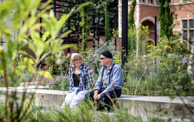 2 mensen zitten op de zitbank in de tuin van het Hof van Busleyden in Mechelen.