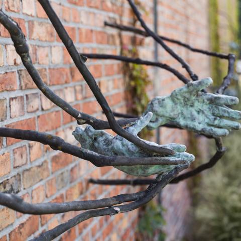 bronzen handen tegen bakstenen muur