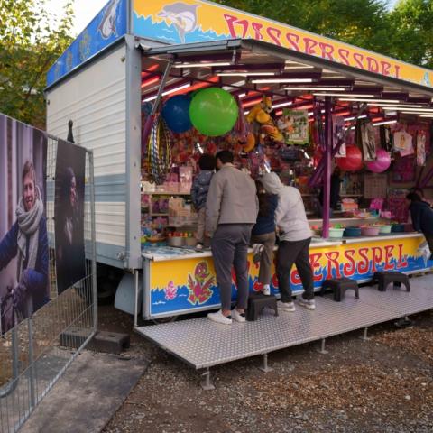 Twee portretten van wijkbewoners uit wijk Arsenaal die tentoongesteld staan naast een kraam op de wijkkermis
