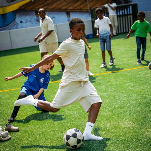 Kinderen spelen op een voetbalveld. Een jongen staat op het punt om tegen de bal te trappen. 