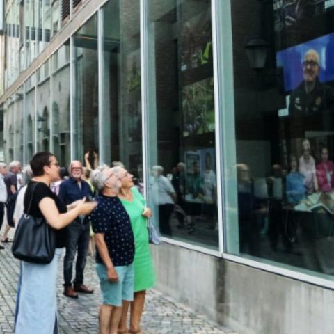 Mensen die naar een fototentoonstelling aan het raam van het Huis van de Mechelaar kijken