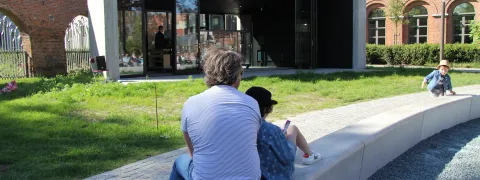 Een vader en zoon zitten op het bankje voor de beiaard in de Sinte-Mettetuin. Ze leunen tegen elkaar.