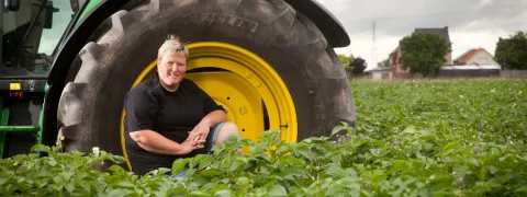 Een persoon zit voor haar tractor op het veld.